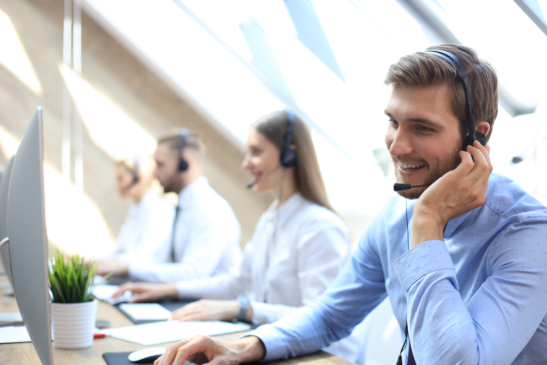 Na imagem a quatro pessoas realizando a prospecção de cliente por telefone. Todos estão sentados, com headphones e olhando para computadores com expressão alegre.