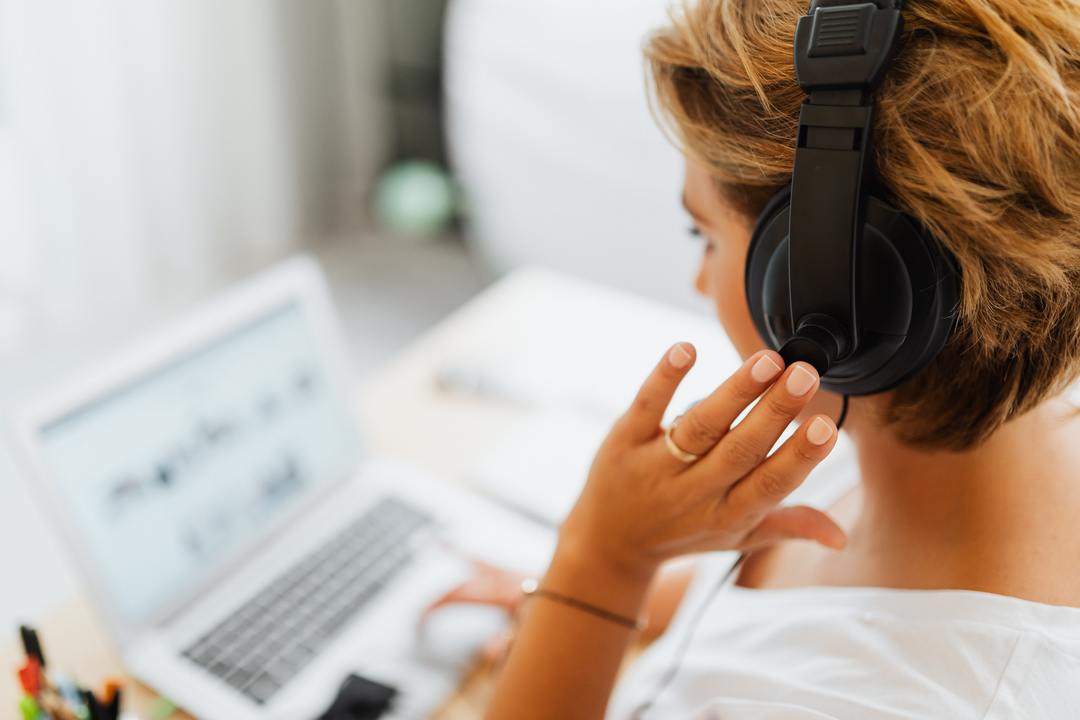 Telefonia para empresa: imagem mostra lateral de costas de mulher com fone de ouvido, de frente para o computador, prestando atendimento telefônico