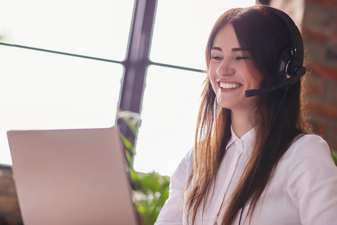 Telefone corporativo: mulher sentada em frente ao computador, com um fone aos ouvidos para realizar o atendimento aos clientes.